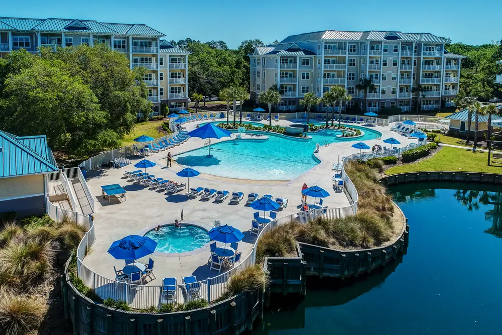 Expansive lagoon-style pool with lazy river, hot tub, and blue umbrella loungers at Bluewater Resort by Spinnaker Resorts, Hilton Head Island, South Carolina.
